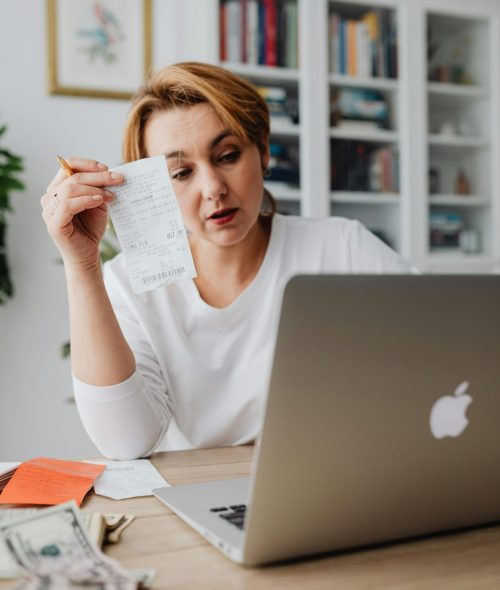 Woman using laptop while managing finances with receipts and cash on the table.